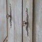 Preview: Detailaufnahme provençalischer Schranktisch — ornamentaler Metallbeschlag mit Schlüsselloch auf grau-blauer Kiefernholzoberfläche, antique opal Finish