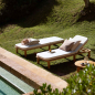 Preview: Zwei Tine K Teak Sonnenliegen am Pool — cremefarbene Kissen, Teak Beistelltisch, Steinmauer im Hintergrund