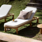 Preview: Tine K Teak Sonnenliege im Garten — cremefarbenes Quick-dry Kissen, verstellbare Rückenlehne, Kissen und Buch als Deko, sonniger Rasen