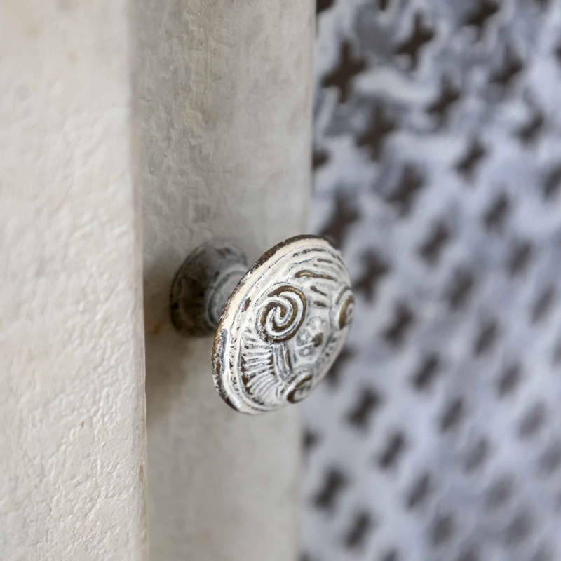 Detailaufnahme reliefierter Metallknauf auf antique crème Kiefernholz — perforierter Metalleinsatz mit Kreuzmuster im Hintergrund