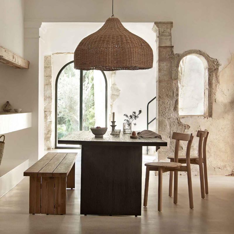 Preview: Tine K Baru Teak Stühle im mediterranen Esszimmer — zwei Stühle am dunklen Tisch, Rattanlampe, Steinwand, natürliches Licht