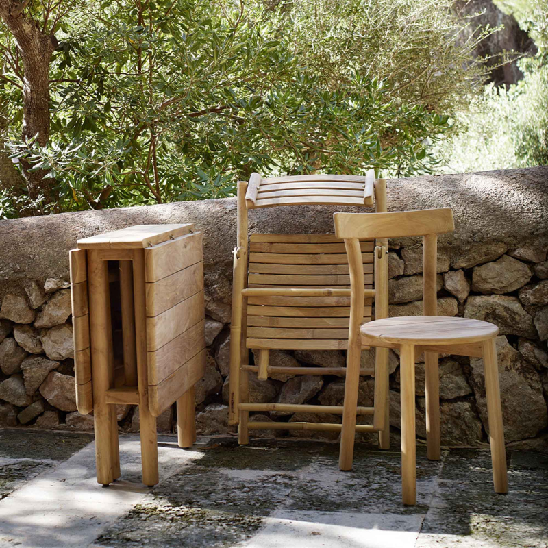 Tine K Baru Teak Stuhl im Außenbereich — kombiniert mit Klapptisch und weiteren Stühlen aus der Baru-Serie, Steinmauer Hintergrund