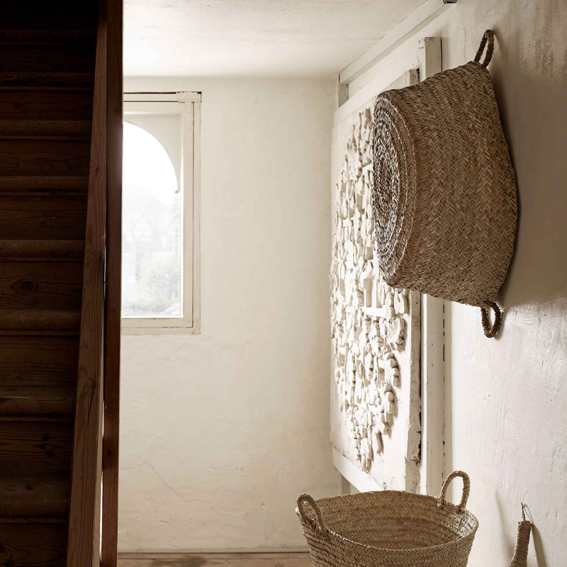 Preview: Tine K Rundkorb aus Palmblatt an weißer Wand hängend — flache Form, 2 Henkel, naturfarbenes Geflecht, mediterranes Interieur