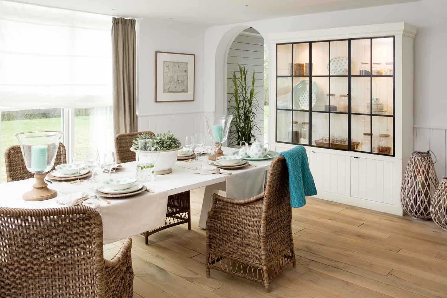 Helles Esszimmer mit dreiteiligem Vitrinenschrank Iron Jason in Weiß und Armlehnstühlen Wexford aus Polyrattan am gedeckten Tisch