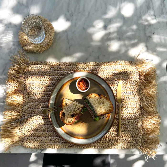 echteckiges Raffia Platzset mit Fransen auf Marmortisch, gedeckt mit Teller, Besteck und Glas im Sonnenlicht