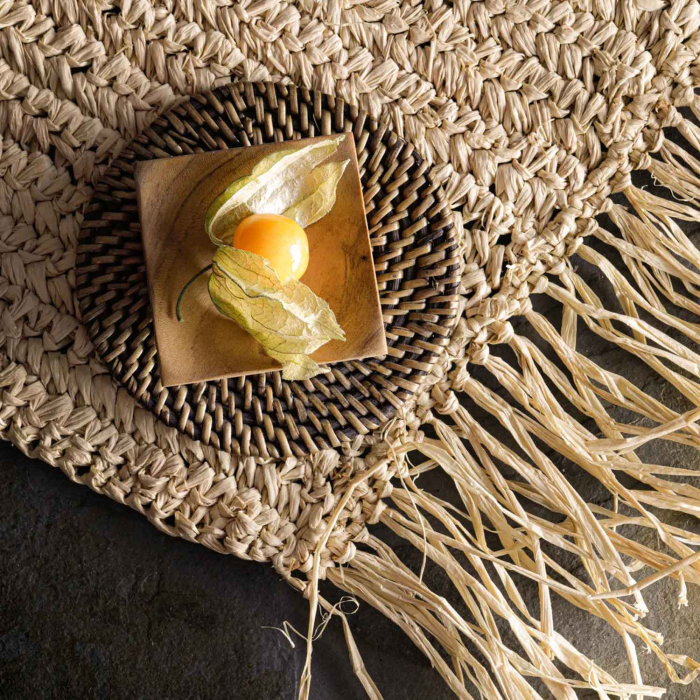 Rundes Raffia-Platzset mit Fransen auf dunklem Stein, mit kleiner Holzschale und Physalis, Detailaufnahme Geflecht