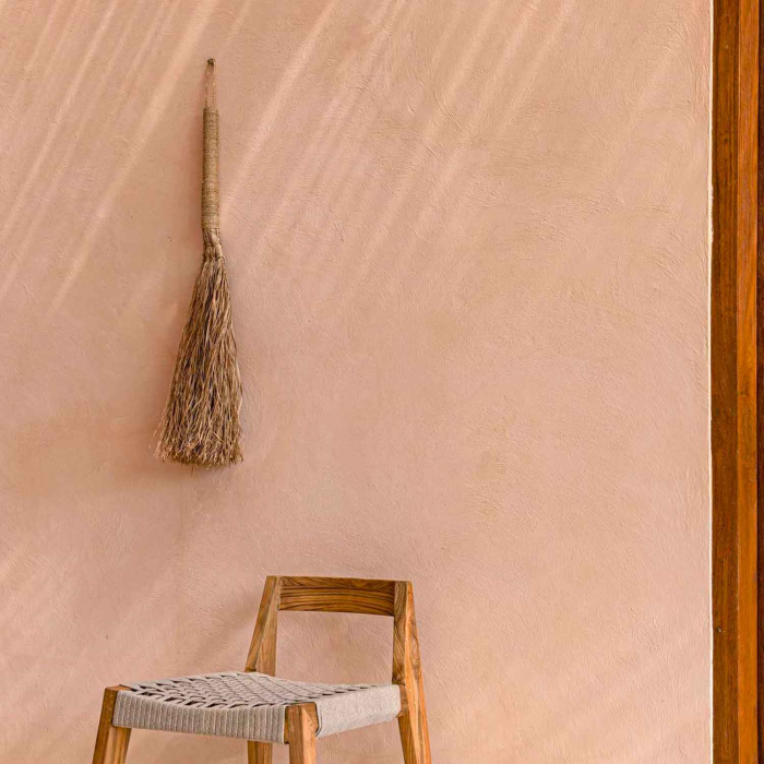 Grumpy Broom an terrakottafarbener Wand hängend, mit Holzstuhl darunter – Ambiente-Aufnahme